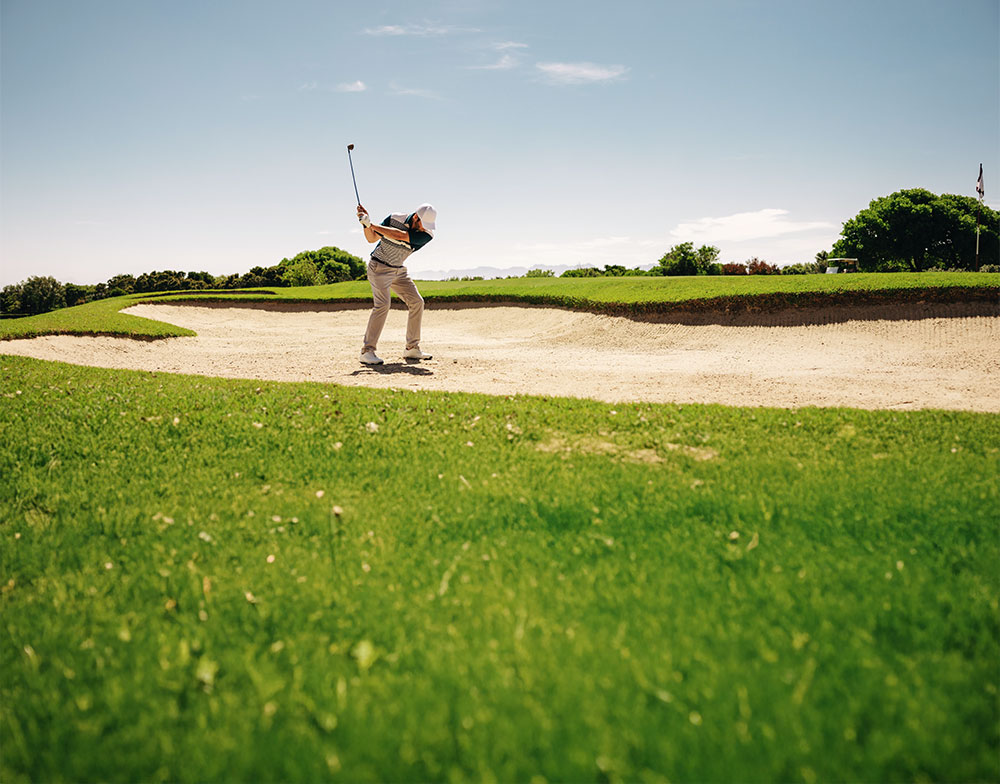 A man getting rid to hit a ball out of the bunker at the golf course